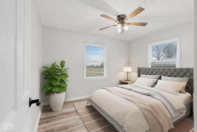 bedroom with a textured ceiling, ceiling fan, light hardwood / wood-style flooring, and multiple windows