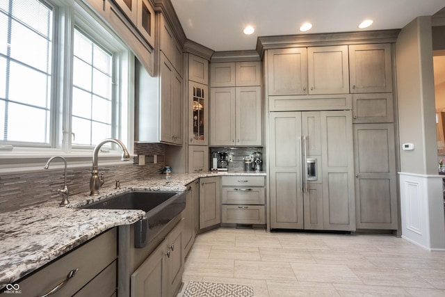 kitchen featuring light stone countertops, backsplash, paneled built in fridge, and sink