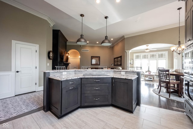 kitchen featuring light stone counters, decorative light fixtures, ceiling fan, and a center island with sink