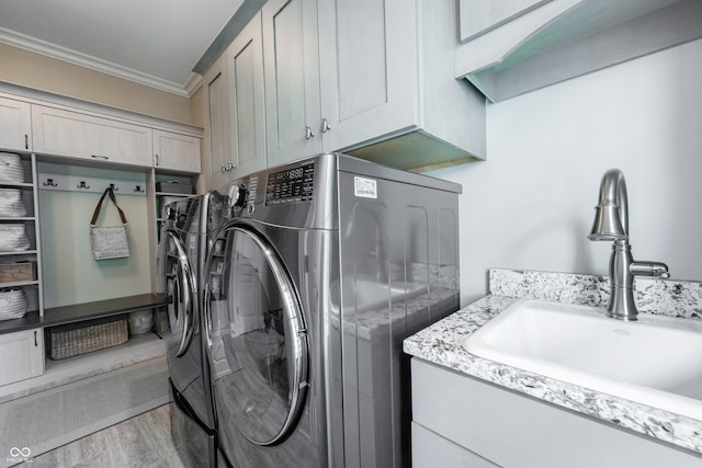 laundry area featuring sink, crown molding, washing machine and dryer, cabinets, and light wood-type flooring