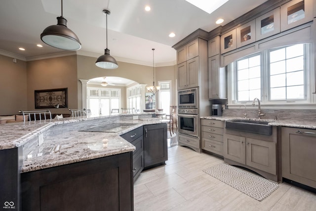 kitchen featuring a large island, sink, stainless steel appliances, light stone countertops, and decorative light fixtures