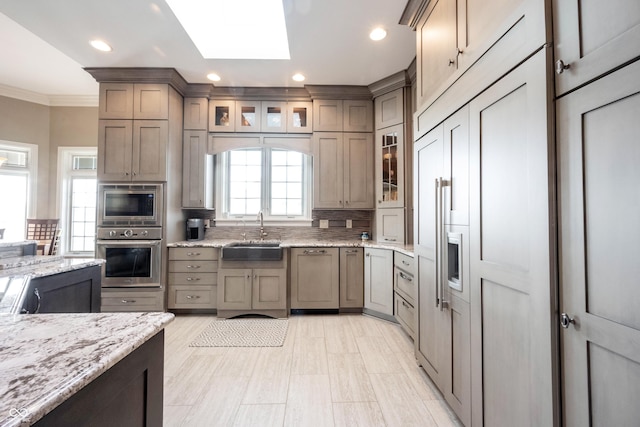 kitchen with sink, crown molding, a skylight, stainless steel appliances, and light stone countertops