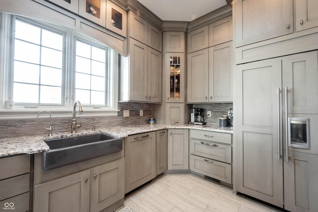 kitchen with dishwashing machine, sink, paneled built in refrigerator, backsplash, and light stone counters