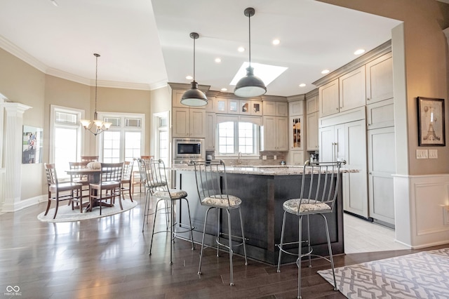 kitchen featuring a spacious island, a breakfast bar area, light stone counters, crown molding, and wood-type flooring