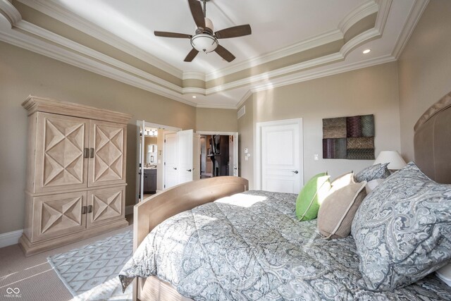 bedroom with a spacious closet, light colored carpet, a tray ceiling, crown molding, and ensuite bath