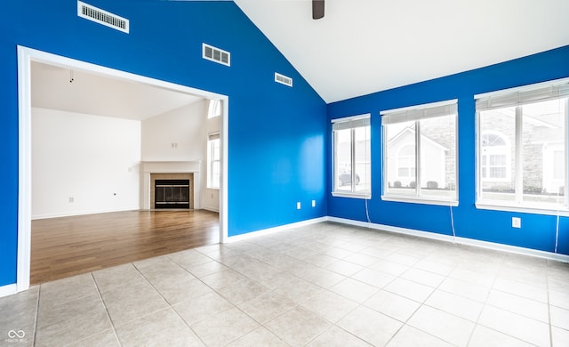 unfurnished living room featuring light hardwood / wood-style flooring, high vaulted ceiling, ceiling fan, and a tiled fireplace