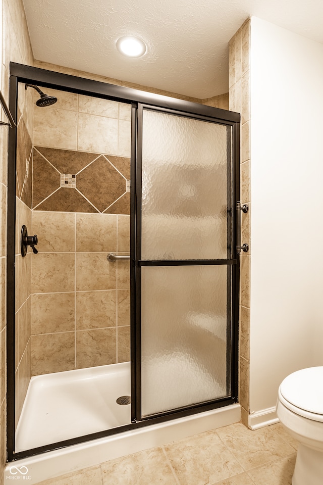 bathroom featuring tile patterned floors, toilet, a shower with shower door, and a textured ceiling