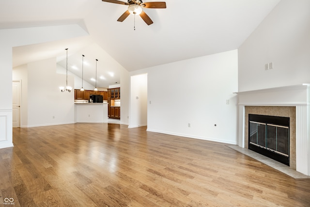 unfurnished living room featuring ceiling fan with notable chandelier, light wood-type flooring, a fireplace, and vaulted ceiling