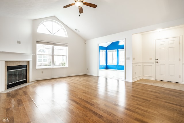 unfurnished living room with a tiled fireplace, ceiling fan, plenty of natural light, and light hardwood / wood-style flooring