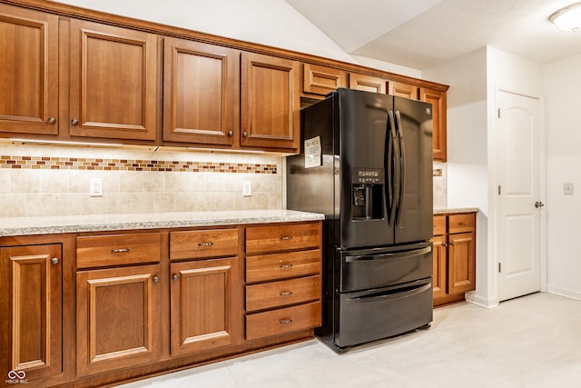 kitchen with black fridge with ice dispenser, light stone countertops, and backsplash