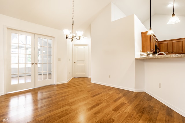 unfurnished dining area featuring hardwood / wood-style flooring, a notable chandelier, french doors, and vaulted ceiling