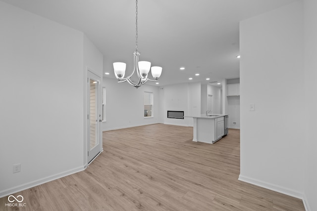 unfurnished living room with light hardwood / wood-style flooring, a notable chandelier, and sink