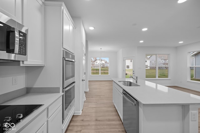 kitchen featuring white cabinetry, sink, stainless steel appliances, and a center island with sink