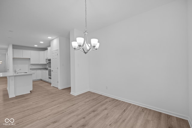 kitchen featuring white cabinetry, an inviting chandelier, an island with sink, decorative light fixtures, and light wood-type flooring