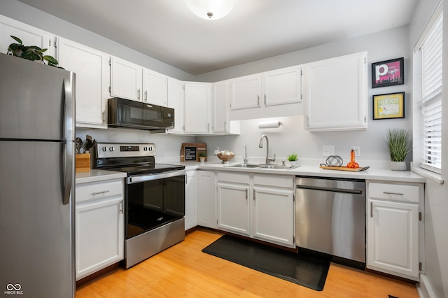 kitchen with appliances with stainless steel finishes, white cabinets, sink, and light hardwood / wood-style floors