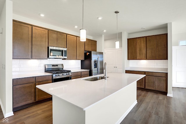 kitchen with tasteful backsplash, a center island with sink, hanging light fixtures, dark hardwood / wood-style flooring, and stainless steel appliances