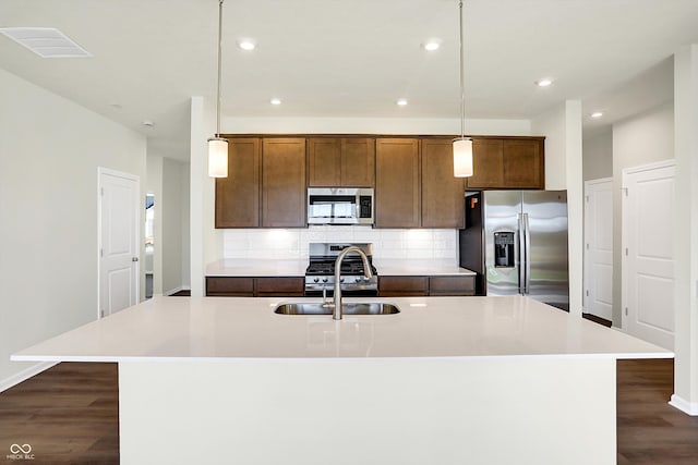 kitchen featuring dark hardwood / wood-style flooring, appliances with stainless steel finishes, an island with sink, pendant lighting, and sink