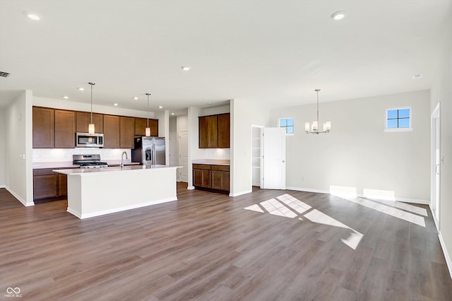 kitchen with an island with sink, hanging light fixtures, stainless steel appliances, and dark hardwood / wood-style floors