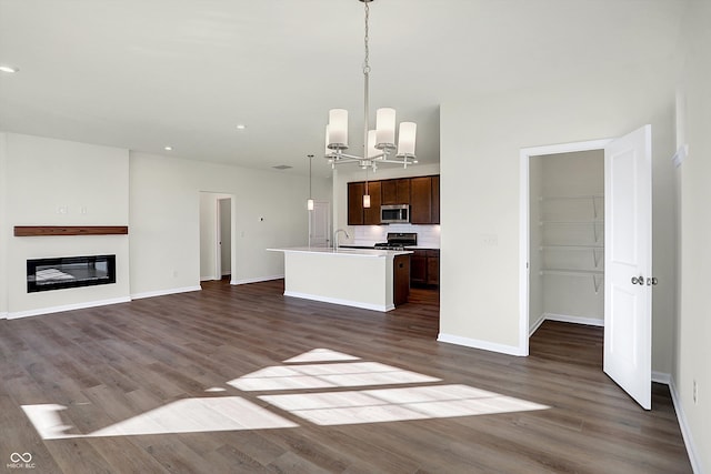 kitchen featuring appliances with stainless steel finishes, decorative light fixtures, an inviting chandelier, dark hardwood / wood-style floors, and a kitchen island with sink