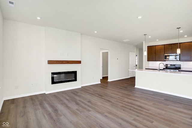 unfurnished living room featuring visible vents, a glass covered fireplace, baseboards, dark wood-style floors, and recessed lighting