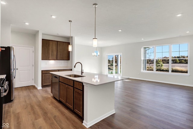 kitchen with wood finished floors, an island with sink, a sink, appliances with stainless steel finishes, and hanging light fixtures
