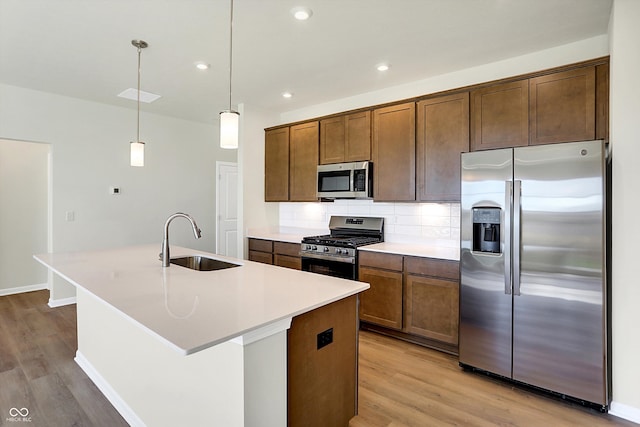 kitchen featuring hanging light fixtures, appliances with stainless steel finishes, a kitchen island with sink, light wood-type flooring, and sink