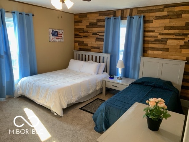 carpeted bedroom featuring ceiling fan, wood walls, and multiple windows