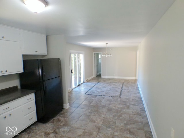 kitchen featuring a notable chandelier, hanging light fixtures, black fridge, and white cabinets