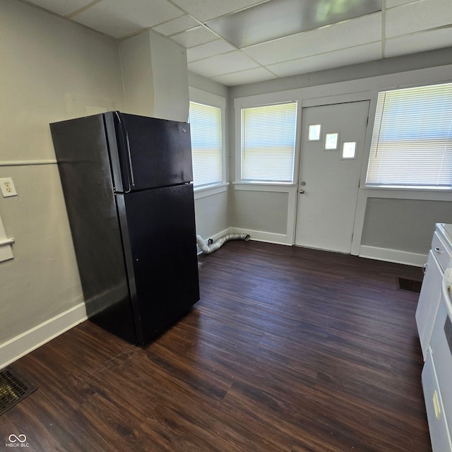 kitchen featuring dark wood-type flooring, a drop ceiling, black fridge, and white cabinets