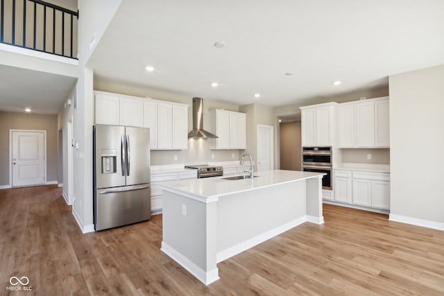 kitchen featuring wall chimney range hood, sink, appliances with stainless steel finishes, light hardwood / wood-style floors, and white cabinetry