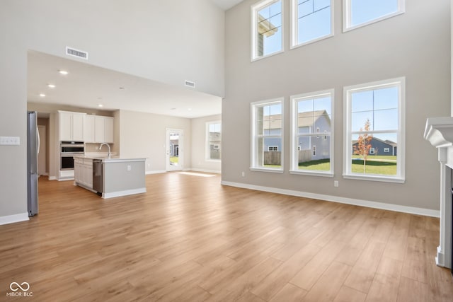 unfurnished living room with a healthy amount of sunlight, light hardwood / wood-style floors, and a towering ceiling