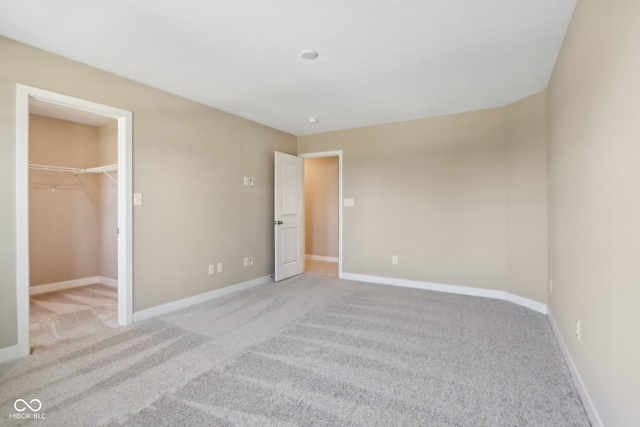 unfurnished bedroom featuring a walk in closet, a closet, and light colored carpet