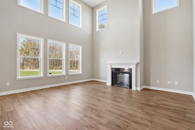 unfurnished living room featuring hardwood / wood-style floors, a towering ceiling, and a healthy amount of sunlight