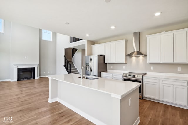 kitchen with stainless steel appliances, white cabinetry, a kitchen island with sink, and wall chimney exhaust hood