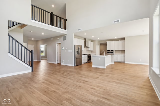 unfurnished living room with light hardwood / wood-style floors, sink, and a high ceiling