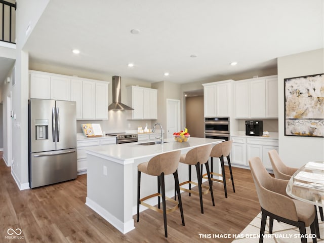 kitchen featuring a center island with sink, wall chimney exhaust hood, white cabinets, and appliances with stainless steel finishes