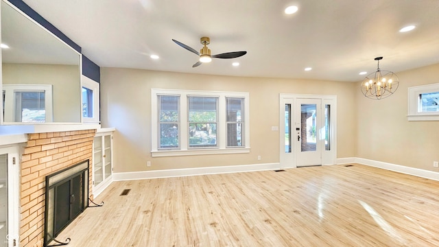 unfurnished living room with a fireplace, ceiling fan with notable chandelier, and light hardwood / wood-style floors