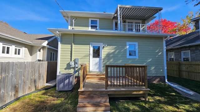 rear view of property featuring central AC unit, a balcony, a wooden deck, and a lawn