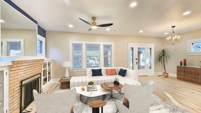 living room featuring light wood-type flooring, ceiling fan with notable chandelier, and a fireplace