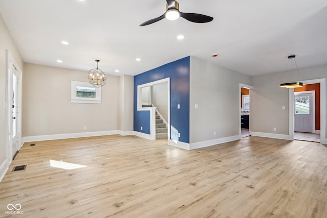 unfurnished living room with ceiling fan with notable chandelier, light hardwood / wood-style floors, and a wealth of natural light