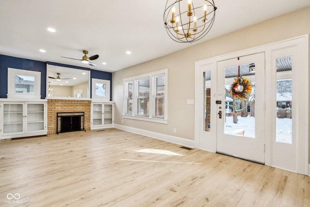 unfurnished living room featuring a brick fireplace, ceiling fan with notable chandelier, and light wood-type flooring