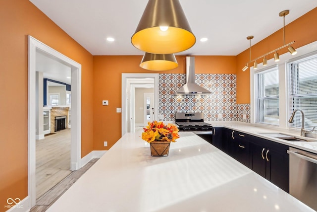 kitchen with sink, wall chimney range hood, backsplash, pendant lighting, and appliances with stainless steel finishes