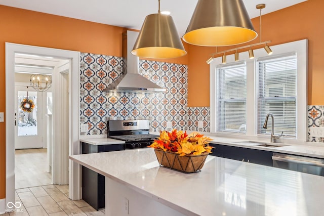 kitchen featuring pendant lighting, appliances with stainless steel finishes, wall chimney exhaust hood, and sink