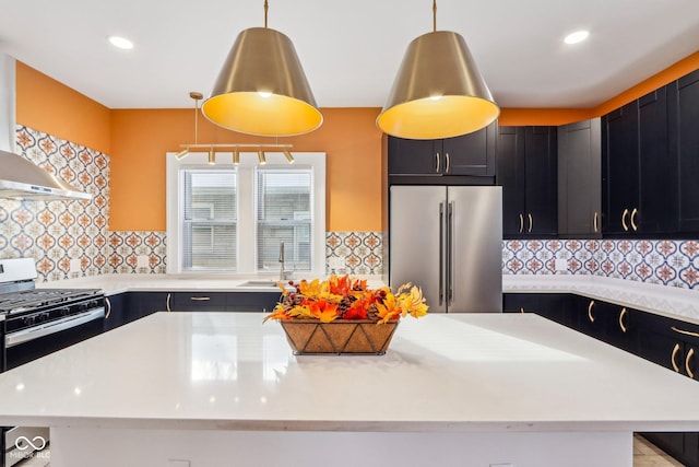 kitchen with high end refrigerator, backsplash, wall chimney range hood, sink, and hanging light fixtures