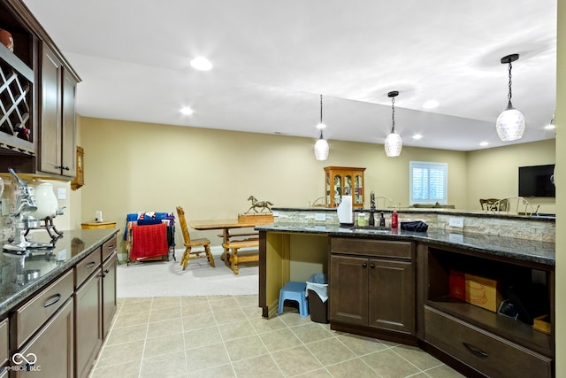 kitchen featuring pendant lighting, dark brown cabinetry, sink, and dark stone counters