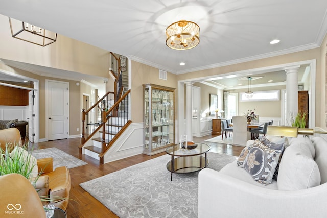 living room featuring hardwood / wood-style flooring, decorative columns, crown molding, and an inviting chandelier