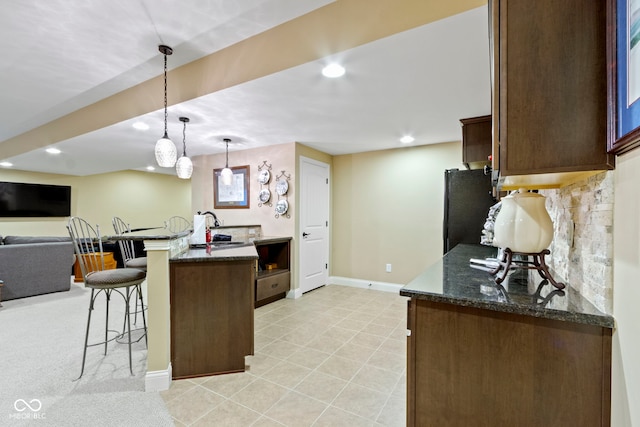 kitchen with sink, hanging light fixtures, a kitchen breakfast bar, dark stone counters, and black refrigerator