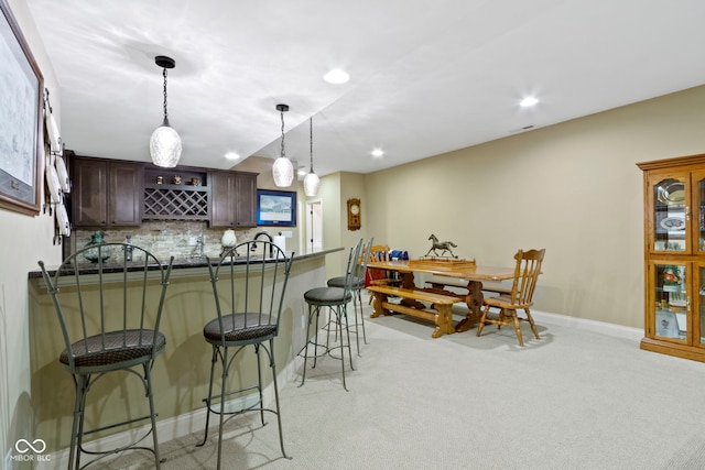 kitchen featuring light carpet, pendant lighting, dark brown cabinetry, and a breakfast bar