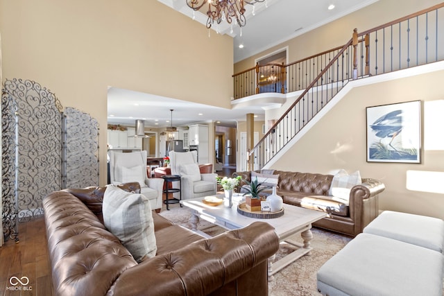 living room with light wood-type flooring, ornamental molding, a towering ceiling, and a notable chandelier