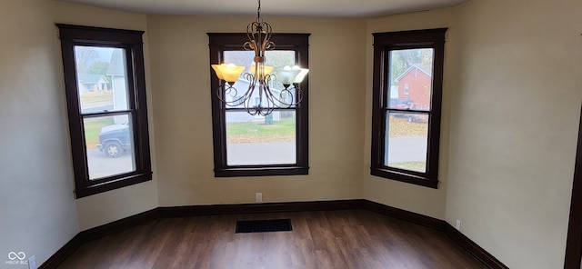 unfurnished dining area with an inviting chandelier, plenty of natural light, and dark hardwood / wood-style flooring